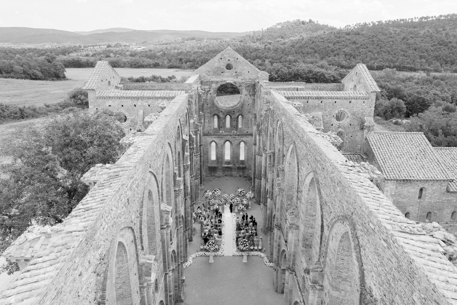Crno-bela fotografija venčanja u ruševinama srednjovekovne crkve u Toskani, snimljena dronom u editorial stilu.
