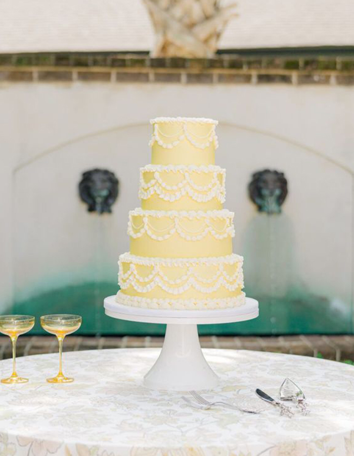 7 Wedding Cake Trends for 2025: Inspiring Designs for Modern Couples 11 Yellow four-tier wedding cake with white vintage-inspired details.