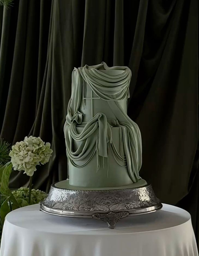7 Wedding Cake Trends for 2025: Inspiring Designs for Modern Couples 4 Green two-tier wedding cake with fondant draping, photographed on a silver plate in front of a green drape.
