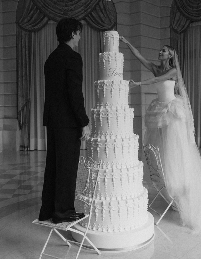 7 Wedding Cake Trends for 2025: Inspiring Designs for Modern Couples 3 editorial style photo of a bride and groom cutting a seven-tier maximalist wedding cake on their wedding day