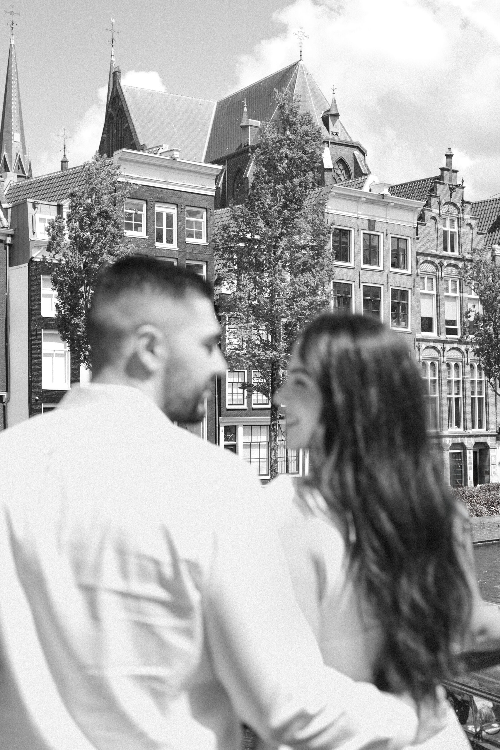 Black and white photo of a couple smiling with famous Amsterdam canal houses in the background