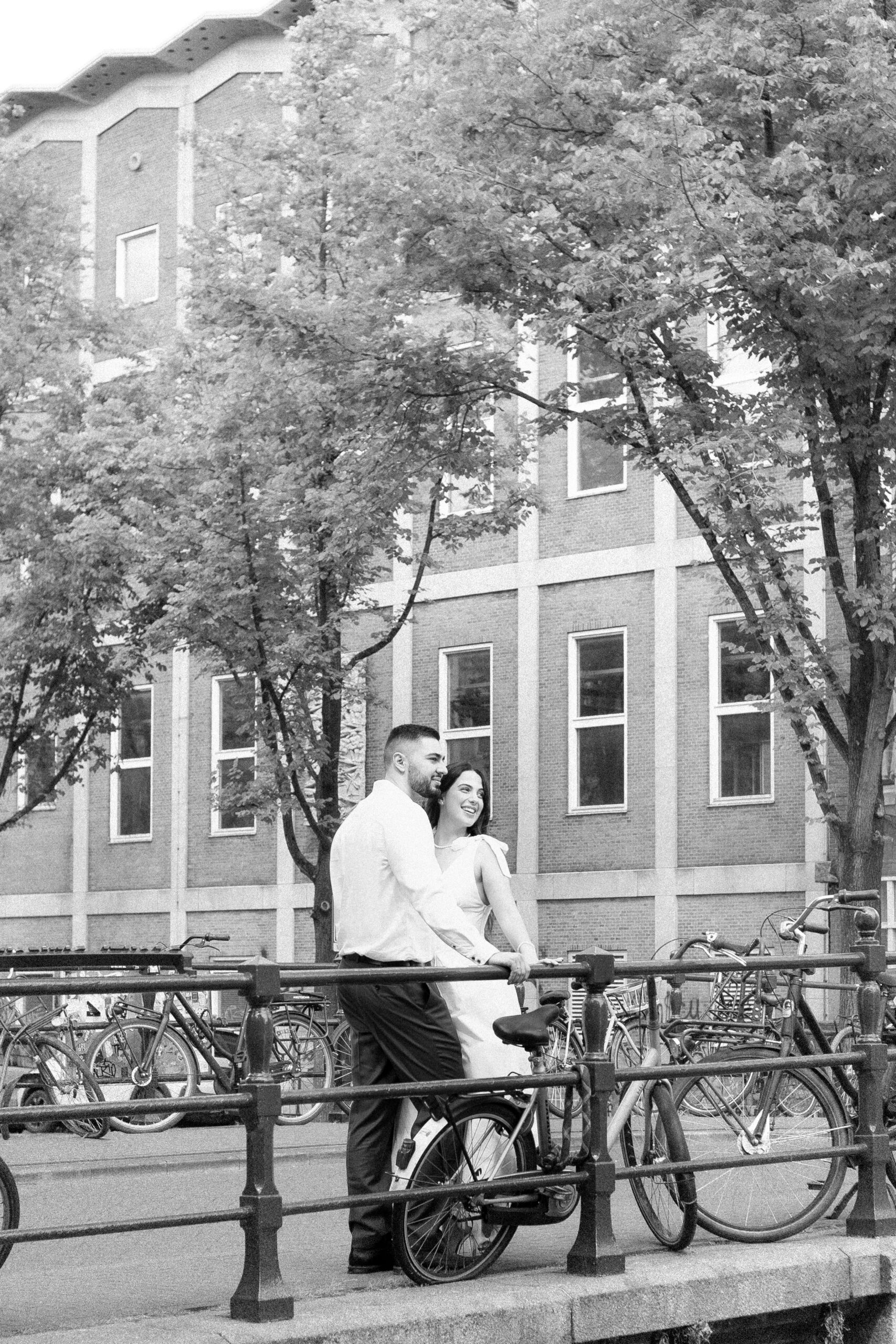 Black and white photo of a bride and groom standing on a bridge over a canal in Amsterdam, looking at a distance
