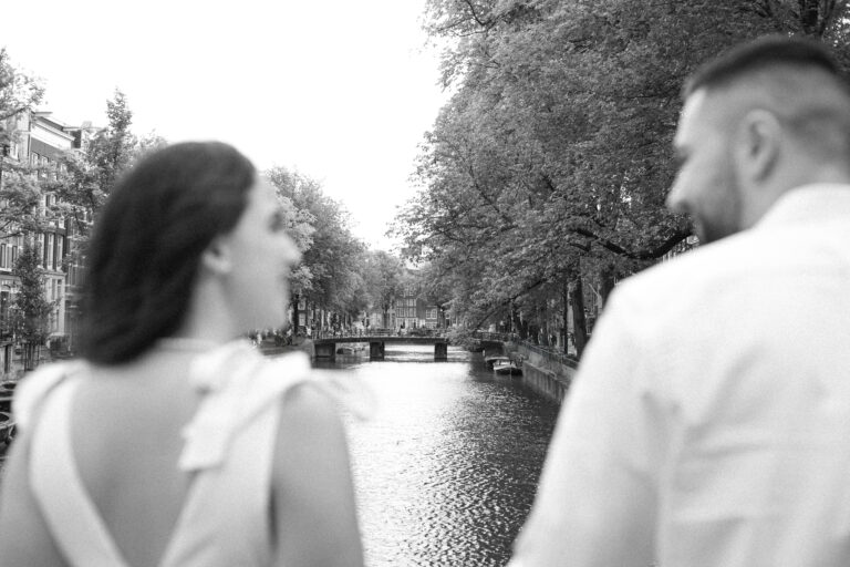 Black and white photo of a bride and groom standing on a bridge over a canal in Amsterdam, looking at each other