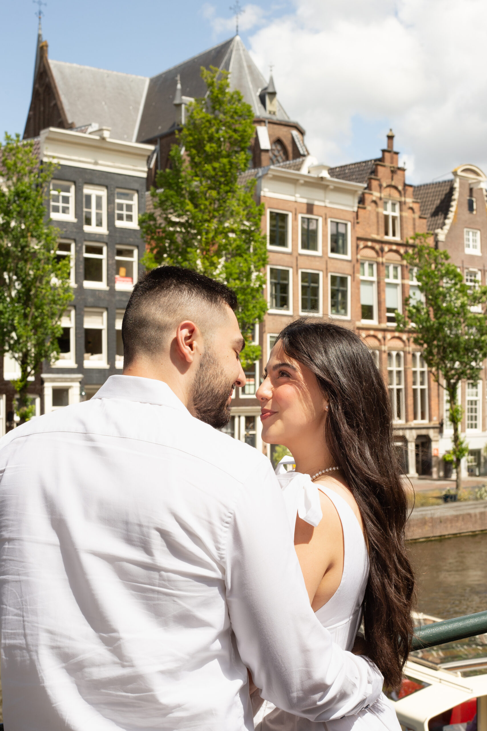 Editorial style photo of a couple looking at each others eyes, with famous Amsterdam canal houses in the background