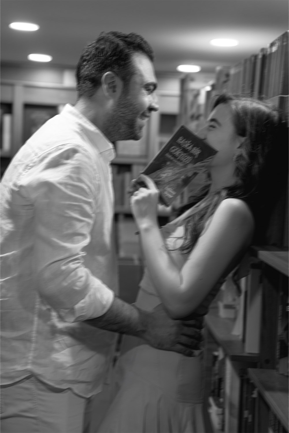 Among the bookshelves of a Belgrade bookstore, a couple shares a playful, affectionate moment, photographed in a black-and-white editorial style that feels cinematic, spontaneous, and romantic.