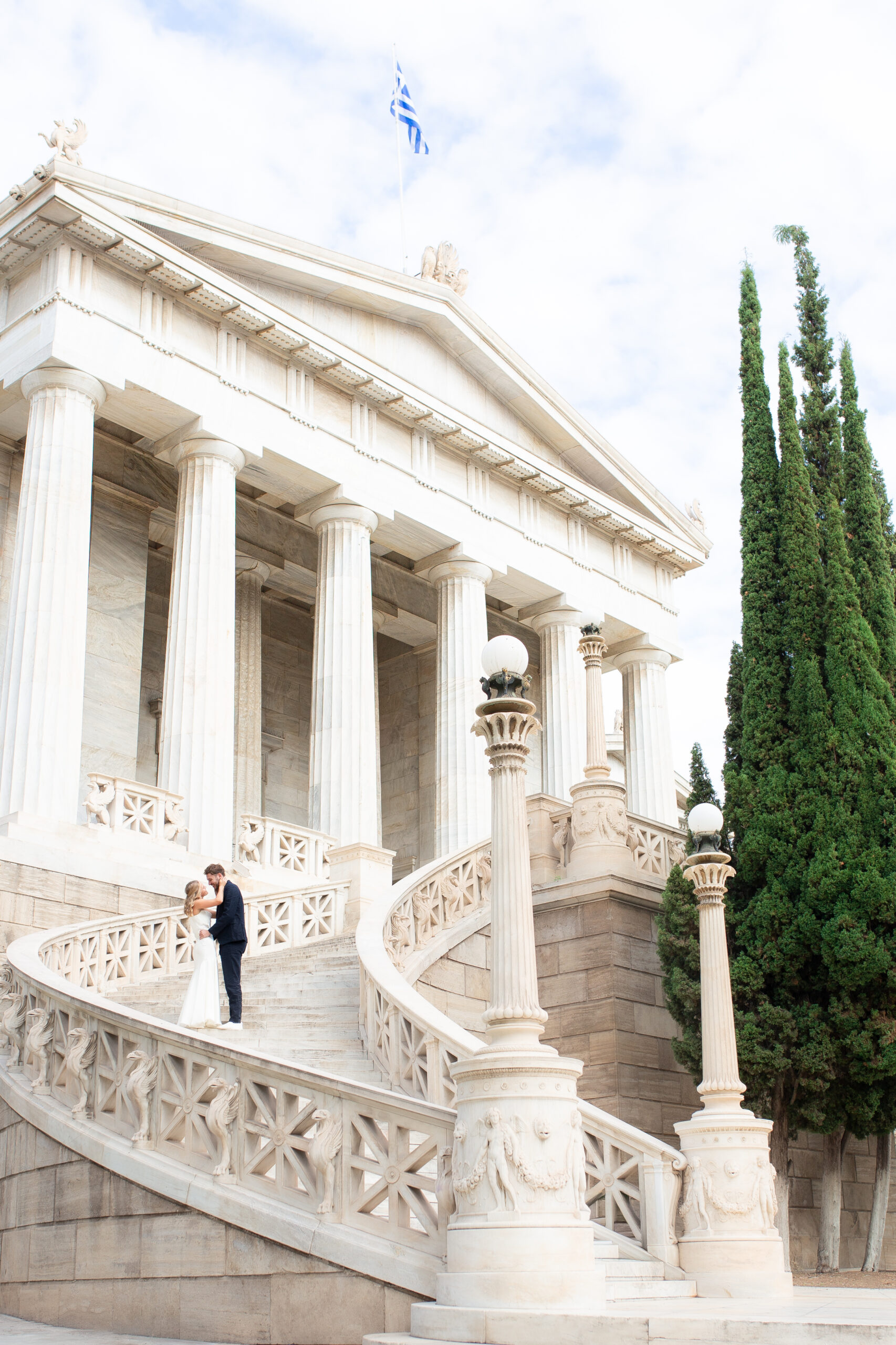 Editorial style photo of the bride and groom standing on the stairs of the Athens National Library in Greece