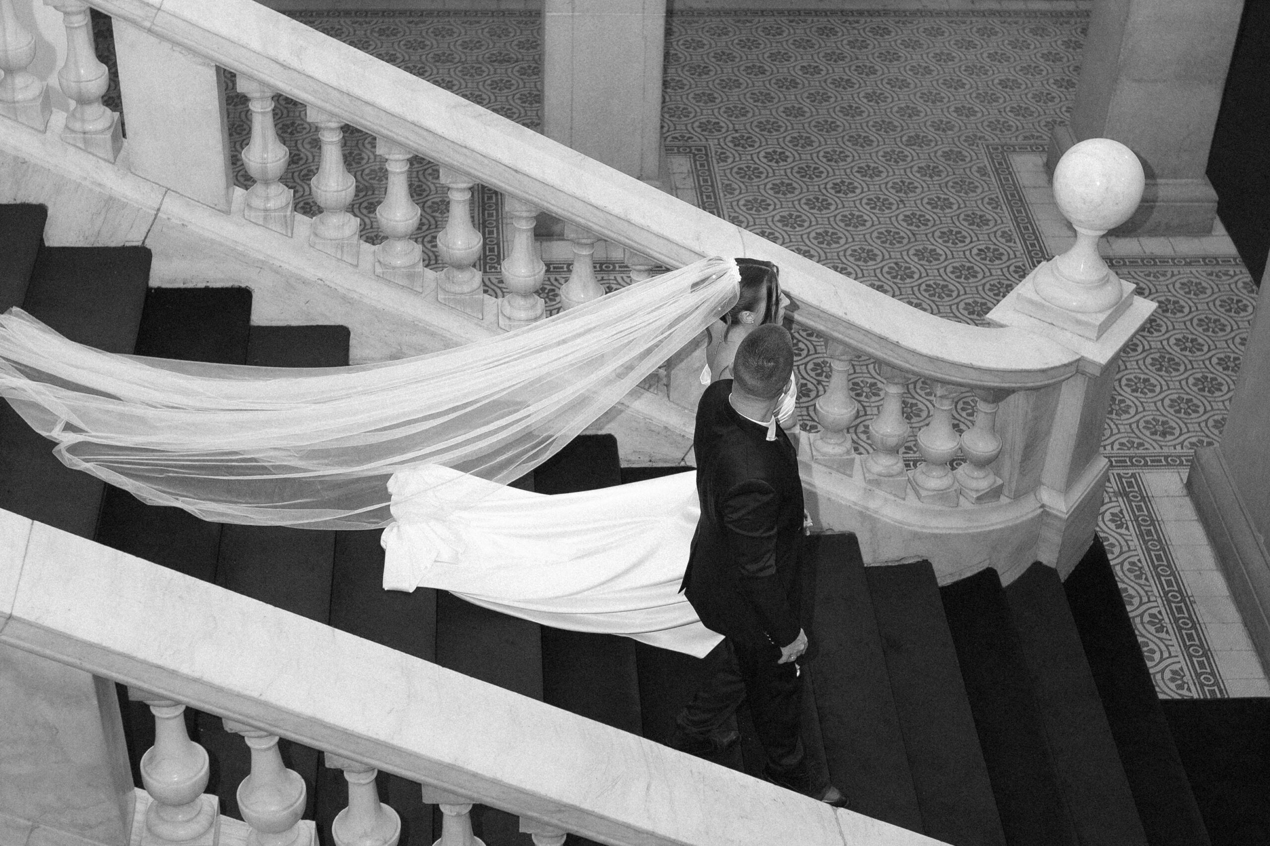 Bride and groom walking down the staircase of a European villa, with veil beautifully following
