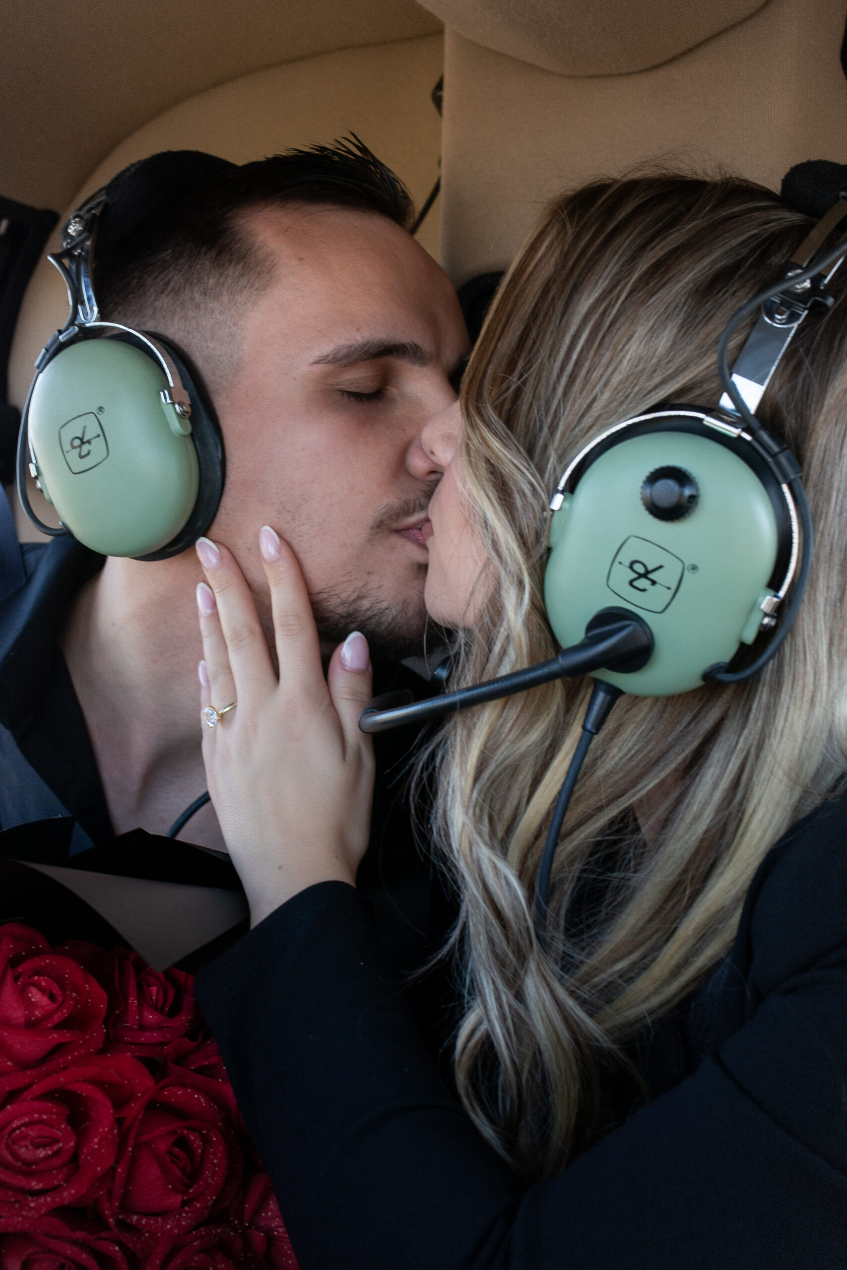 A couple kissing inside the helicopter while wearing headsets, the woman’s engagement ring visible on her hand.