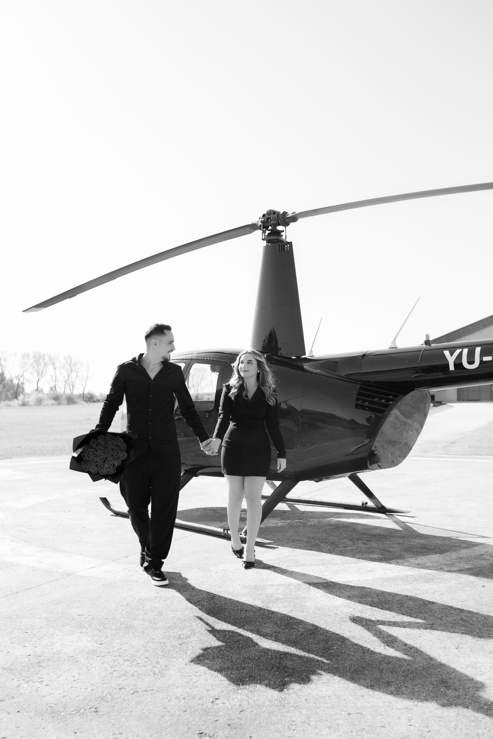 A couple walking out of a helicopter, hand in hand, with the woman looking toward the camera.