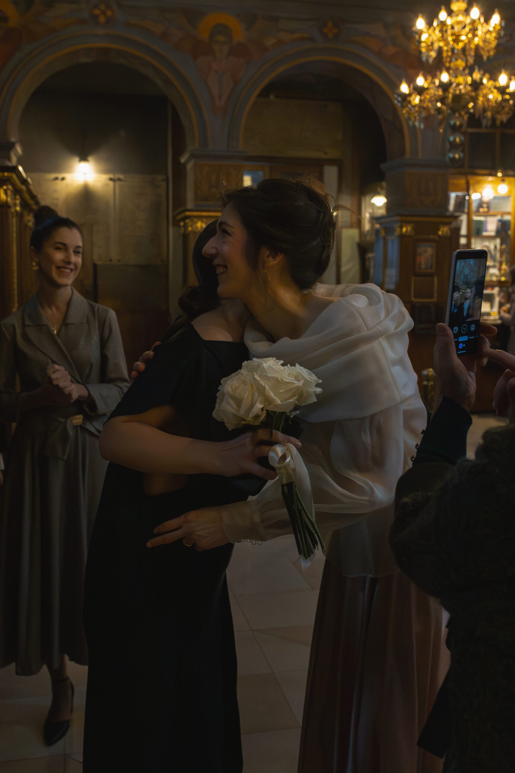 Crkveno venčanje u Vaznesenjskoj crkvi u Beogradu – mlada prima čestitke u crkvi držeći buket belih ruža, pravoslavna svadbena ceremonija