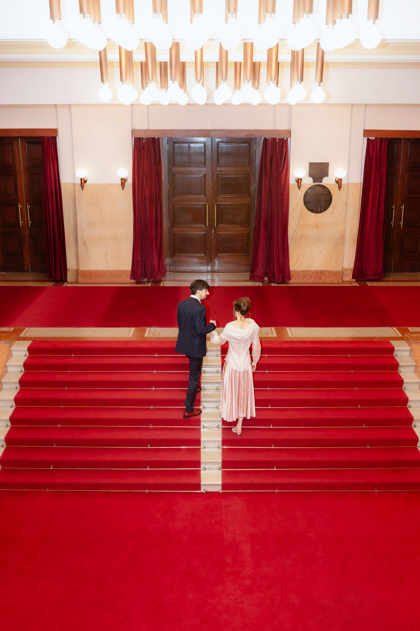 Mladenci se penju crvenim stepenicama Kolarčeve zadužbine, post-wedding photoshoot u Beogradu sa naglašenom simetrijom i elegancijom.