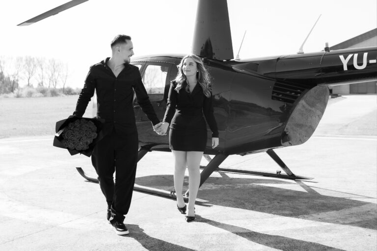 A couple walking out of a helicopter, hand in hand, with the woman looking toward the camera.