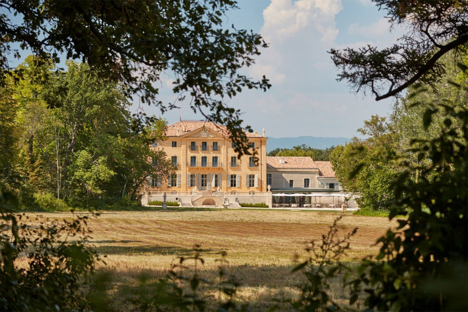 In the French countryside, a château is framed by trees and fields under golden light in a serene, storytelling editorial style.
