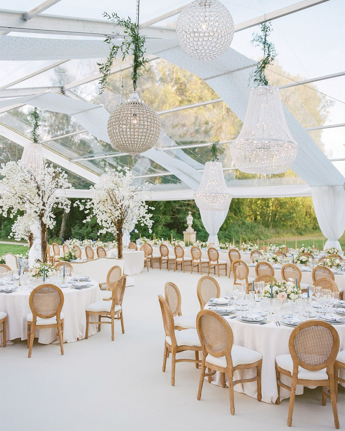 In Provence, a mirrored reception table stretches toward a flower-covered ceremony arch in front of a château in a luxurious editorial wedding style.
