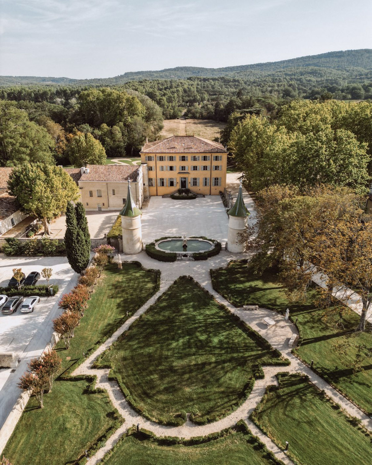 From above in Provence, a grand château and formal gardens unfold symmetrically with tree-lined paths in a timeless editorial style.