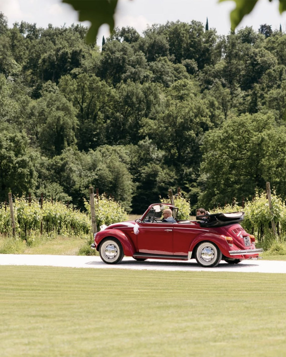 Tenuta Serradesca, Bergamo – couple driving a vintage red convertible through vineyard-lined roads in a relaxed, editorial wedding moment.