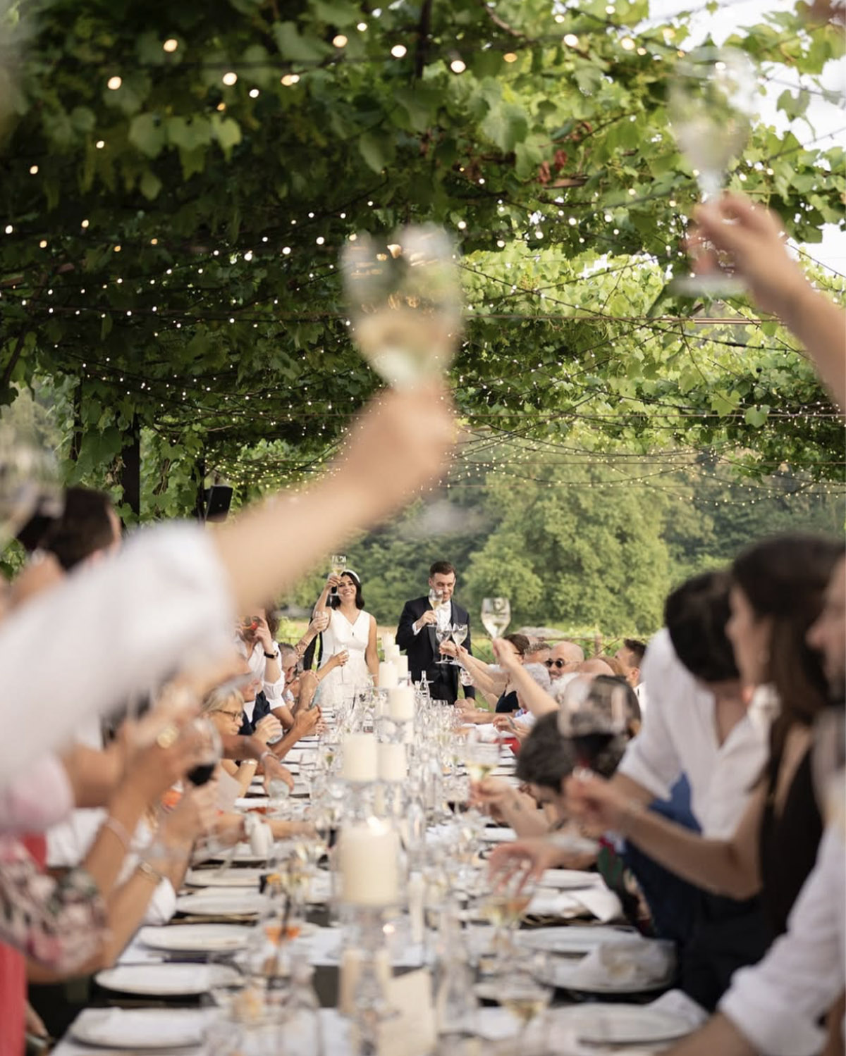 Tenuta Serradesca, Bergamo – long outdoor wedding dinner under vine-covered pergola with string lights, captured in a natural and elegant editorial style.