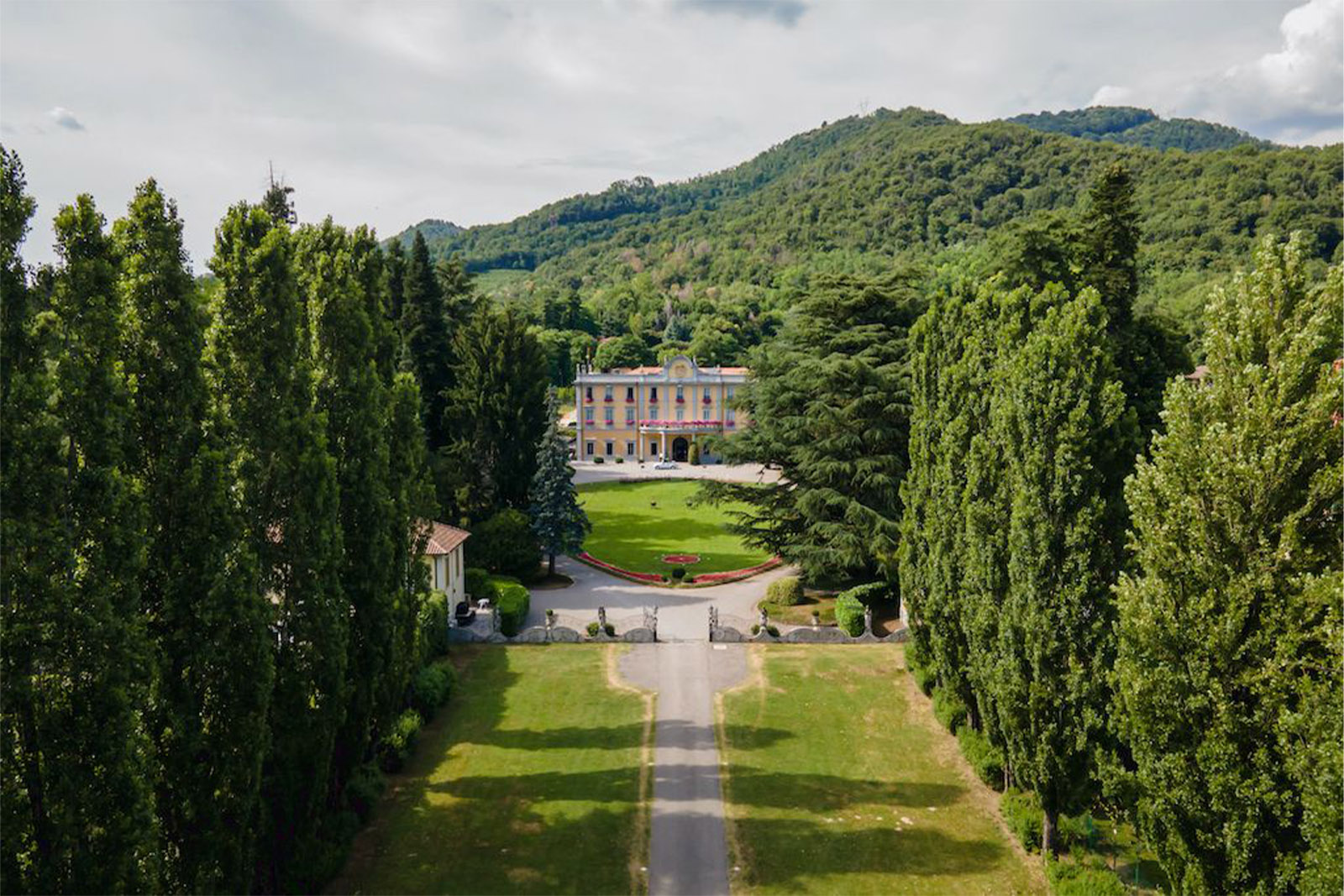 Bergamo, Italy countryside villa framed by tall cypress trees and rolling green hills, captured in a wide editorial aerial style with soft natural light.