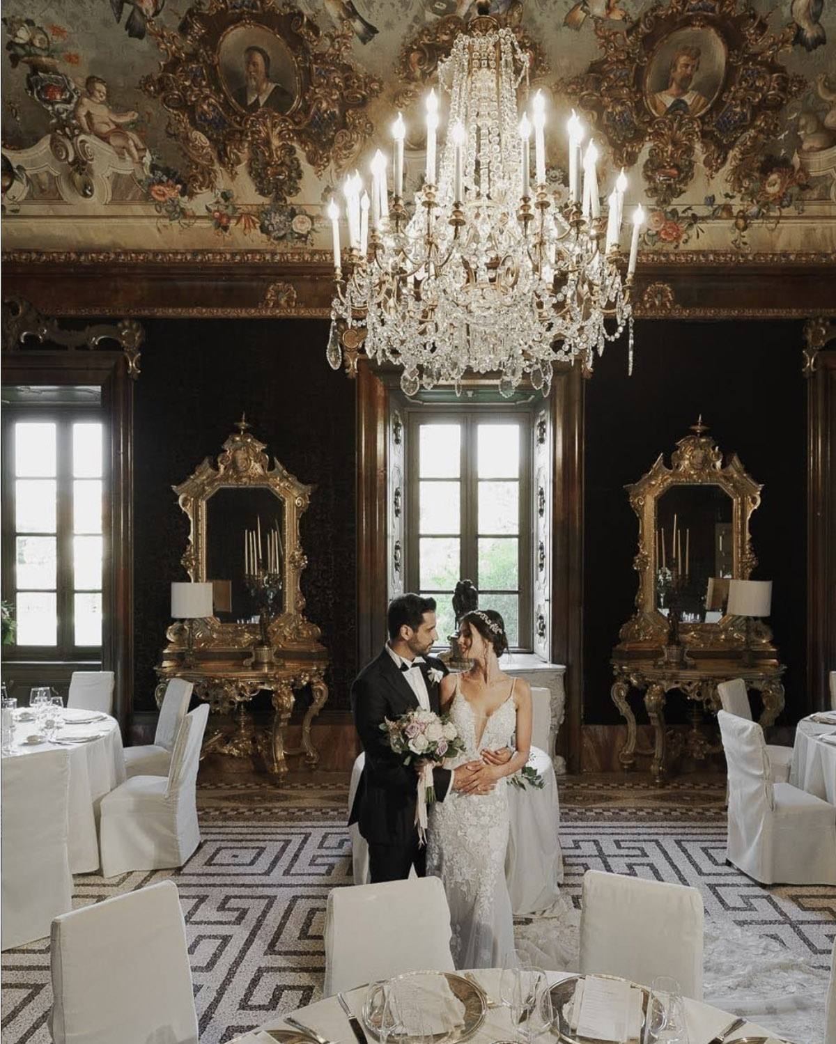 Bergamo, Italy ornate baroque interior with a couple standing beneath a crystal chandelier, captured in a luxurious editorial wedding portrait style.