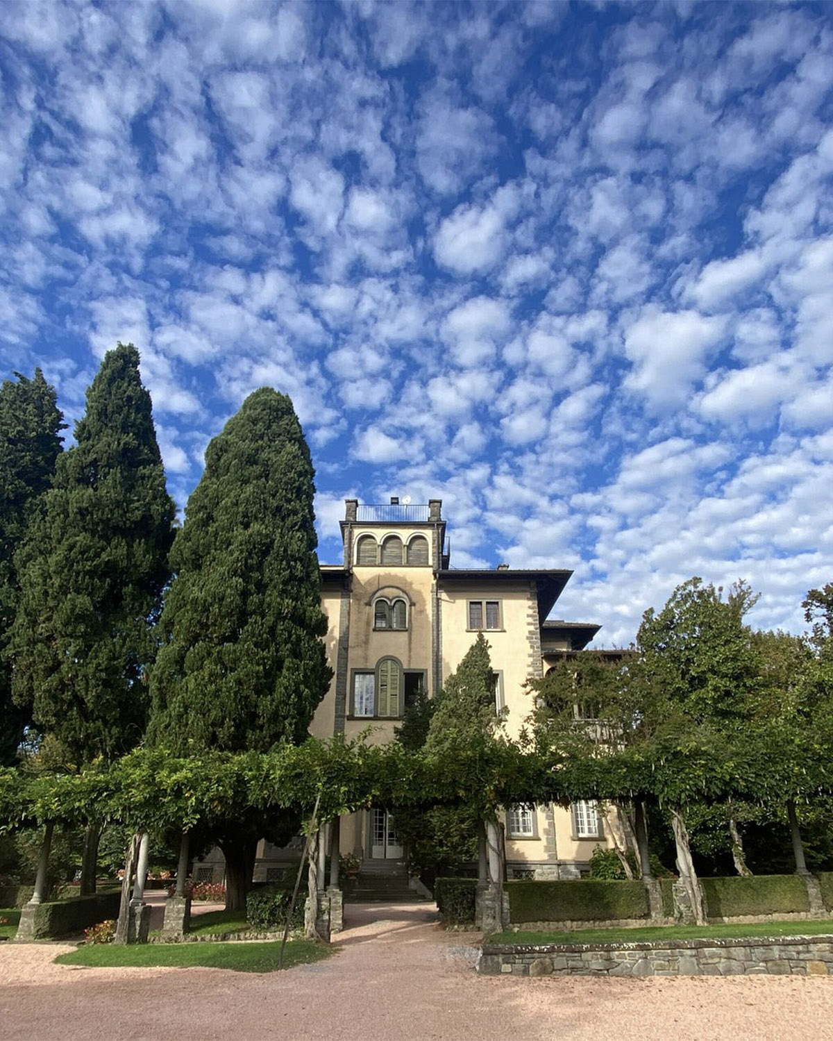 Bergamo, Italy charming villa surrounded by gardens and trees under a textured blue sky, photographed in a relaxed editorial travel style.