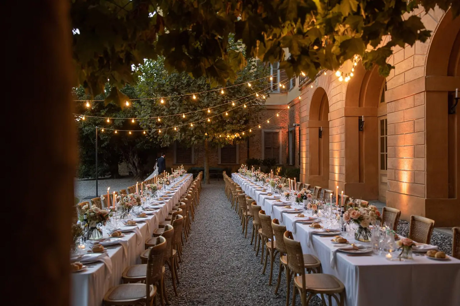 At an Italian villa in Bergamo, two long candlelit reception tables run parallel under warm string lights in an intimate courtyard, photographed in a soft editorial style.