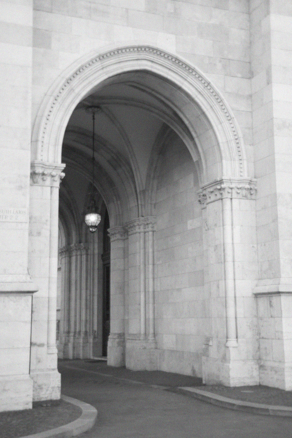 At a grand historic building in Budapest, a vaulted stone corridor with arches and columns is photographed in soft monochrome tones, giving a classic editorial feel.