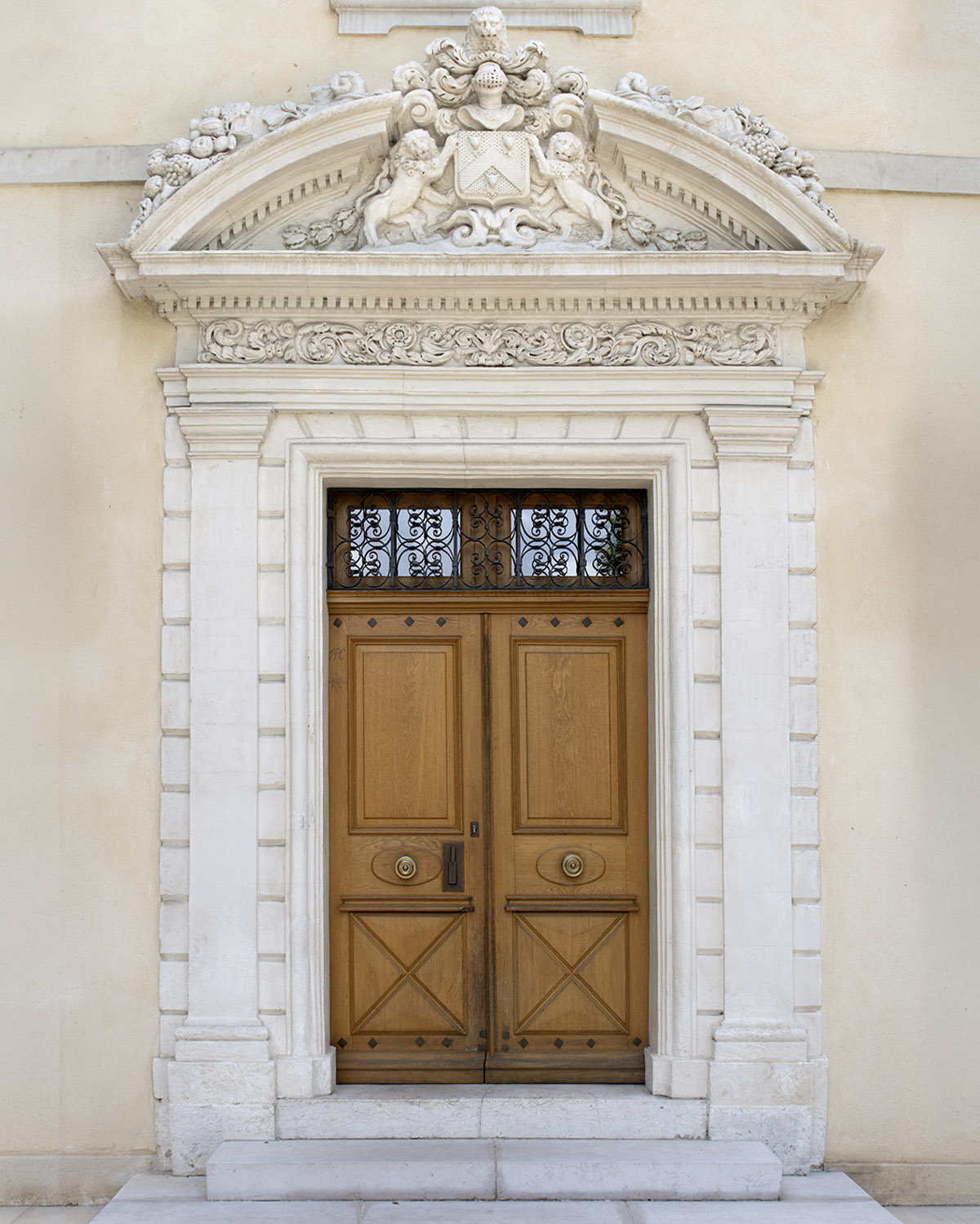 In Provence, France, an ornate carved stone doorway frames tall wooden double doors, captured in a refined architectural editorial style that highlights classical detailing and symmetry.