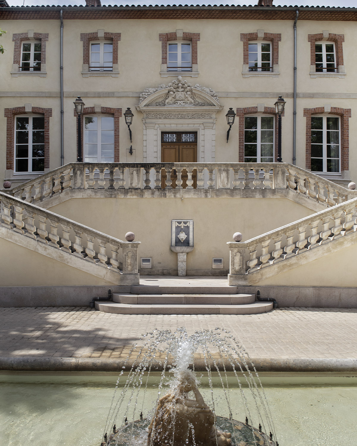 At a château in Provence, a grand symmetrical façade with stone staircases and a central fountain is photographed in a classic architectural editorial style that emphasizes balance and heritage.