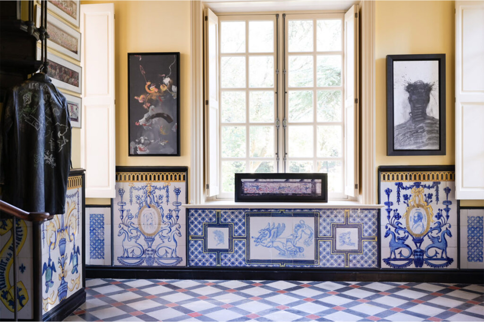 Inside a château room in Provence, patterned tile walls, framed artwork, and a bright window create a refined yet artistic atmosphere, captured in a curated interior editorial style.