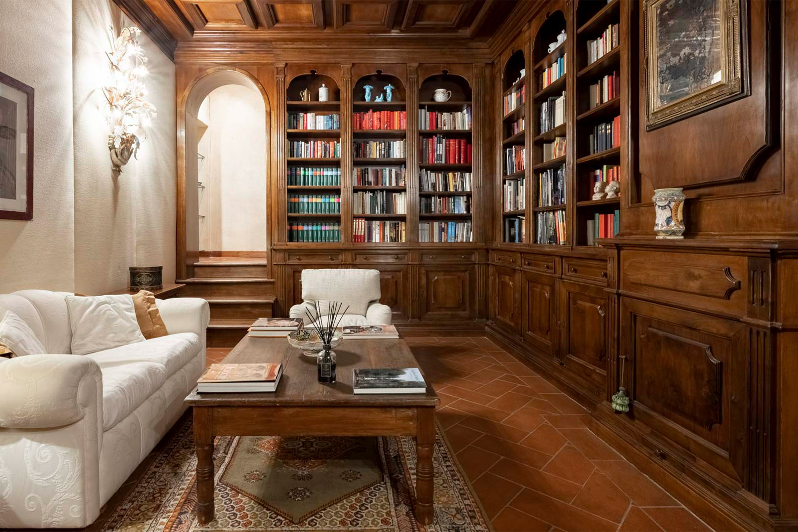 A classic library room inside a Tuscan estate features floor-to-ceiling wooden bookshelves, warm lighting, and plush seating, photographed in an elegant, editorial interior style.