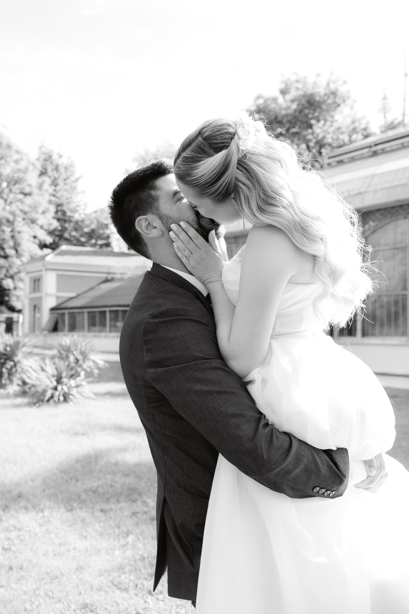 Photoshoot in Jevremovac Botanical Garden, Belgrade | Editorial Post-Wedding Photography 17 Belgrade Botanical Garden greenhouse, a newlywed couple share a kiss while embracing outdoors in front of the glasshouse, captured in an intimate black-and-white editorial style.