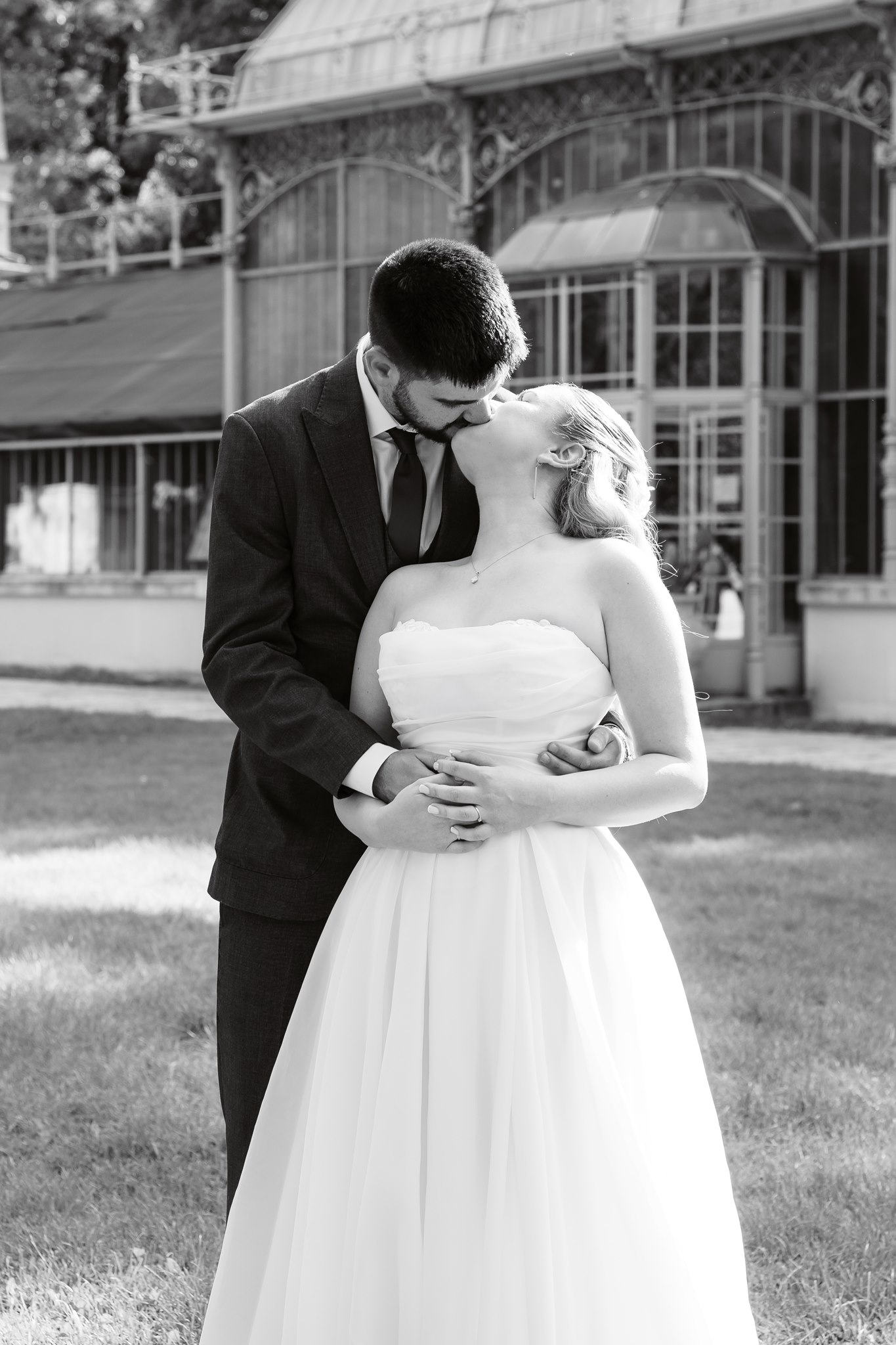 Photoshoot in Jevremovac Botanical Garden, Belgrade | Editorial Post-Wedding Photography 21 Belgrade Botanical Garden greenhouse, a couple share a kiss in front of the ornate glasshouse facade, captured in a classic black-and-white editorial wedding portrait style.