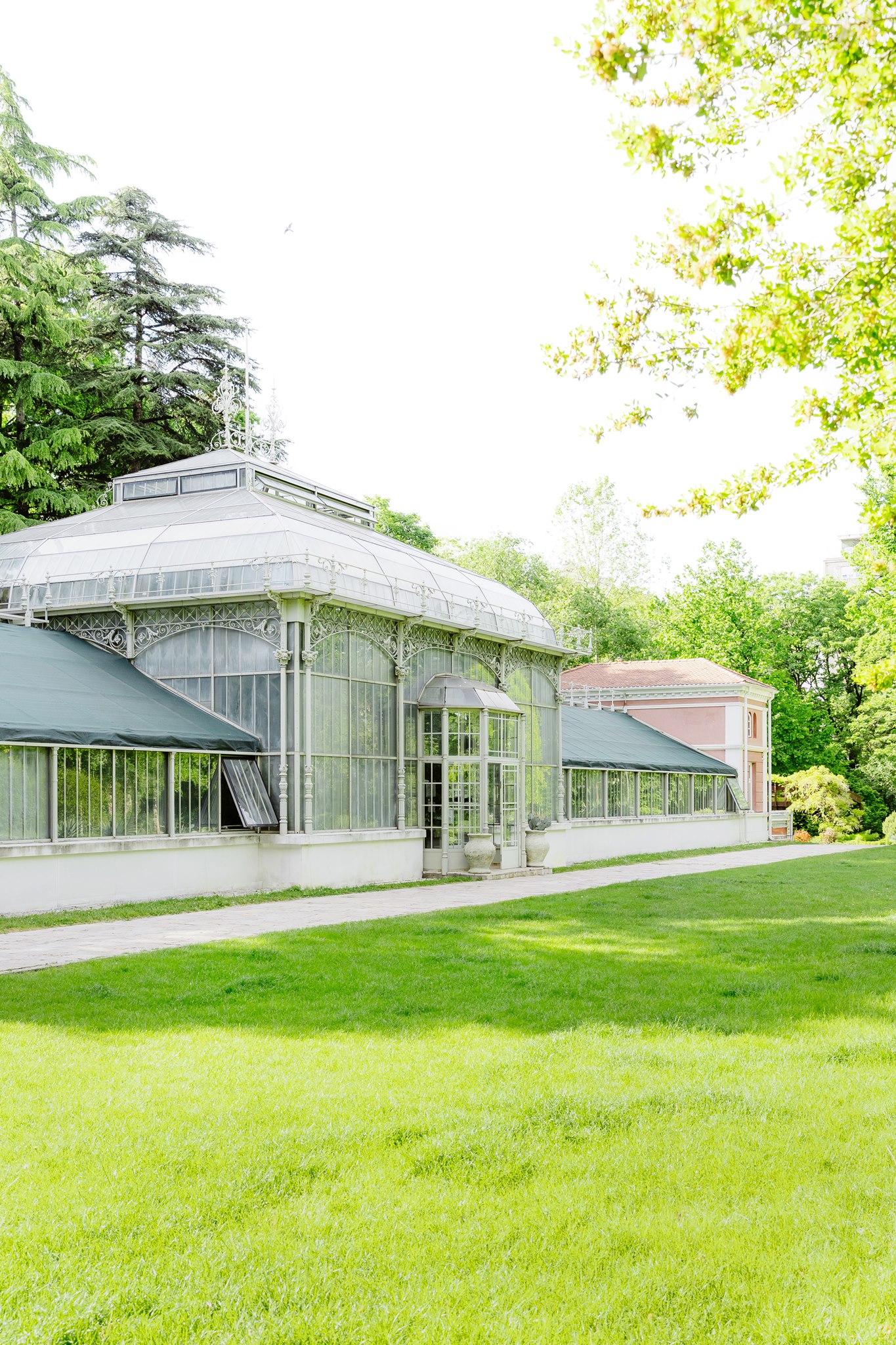 Photoshoot in Jevremovac Botanical Garden, Belgrade | Editorial Post-Wedding Photography 8 Wide editorial shot of the historic Victorian greenhouse at the Jevremovac Botanical Garden in Belgrade, framed by vivid green lawn and spring foliage.