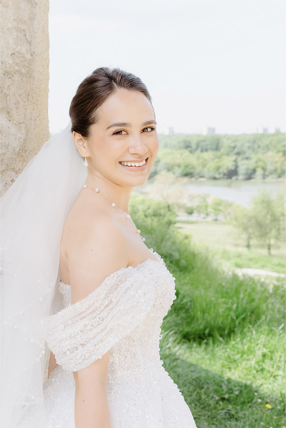 At Kalemegdan Fortress in Belgrade, the bride smiles toward the camera with the river and greenery behind her in a soft and airy editorial bridal portrait.