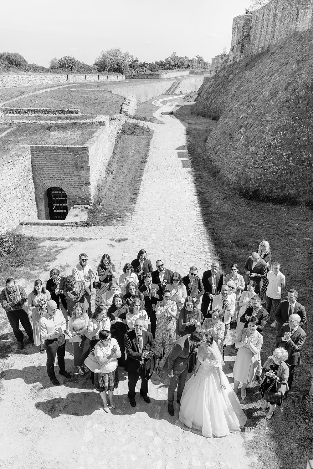 At Kalemegdan Fortress in Belgrade, wedding guests gather around the newlyweds on the fortress grounds in a timeless black-and-white editorial group portrait.