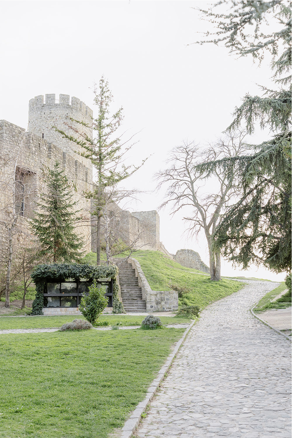 At Kalemegdan Fortress in Belgrade, a winding cobblestone path curves between historic fortifications in a bright editorial landscape photograph of the wedding venue.
