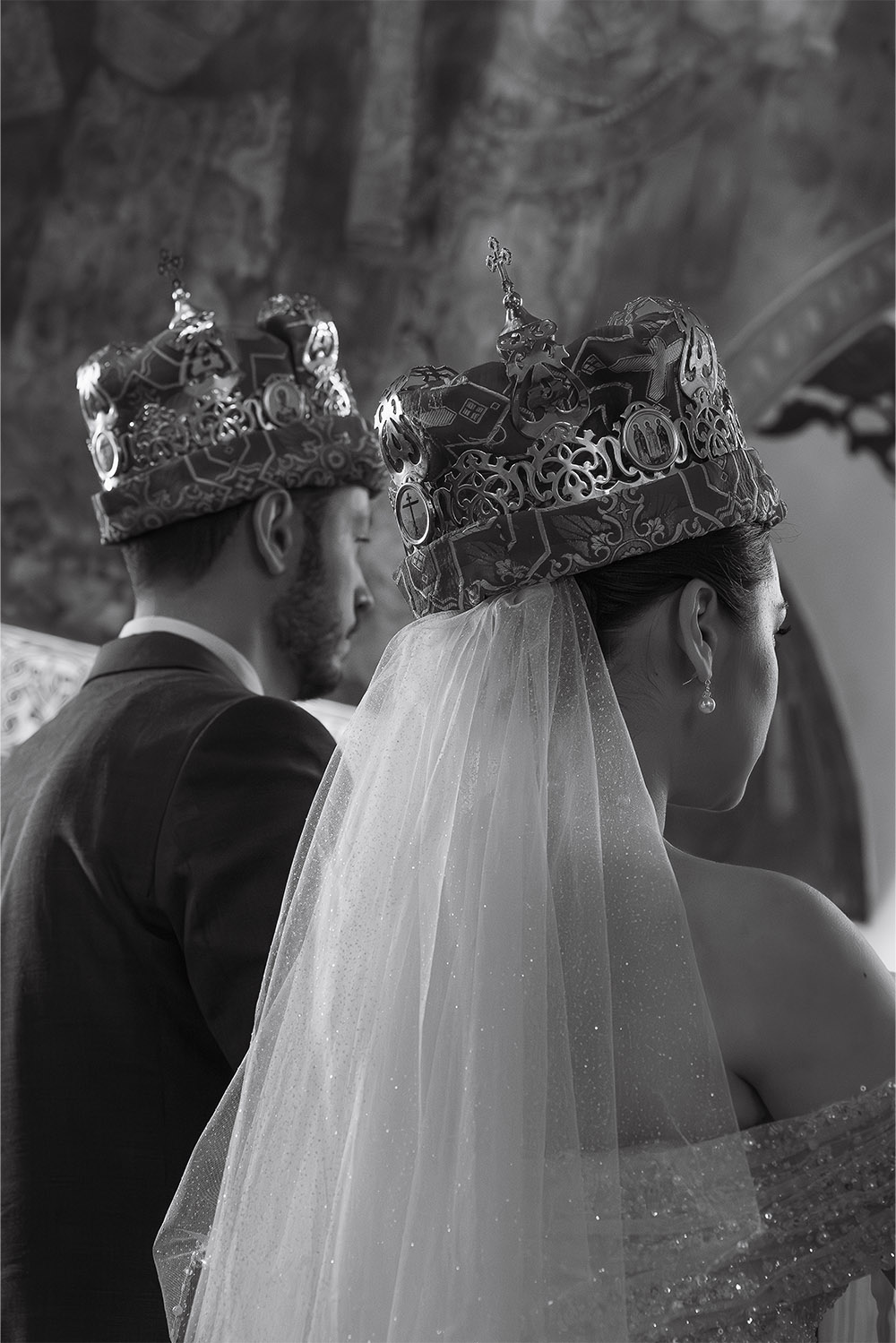 Inside Ružica Church at Kalemegdan Fortress, a bride and groom wear traditional Orthodox wedding crowns during their ceremony in a timeless black-and-white editorial photograph.