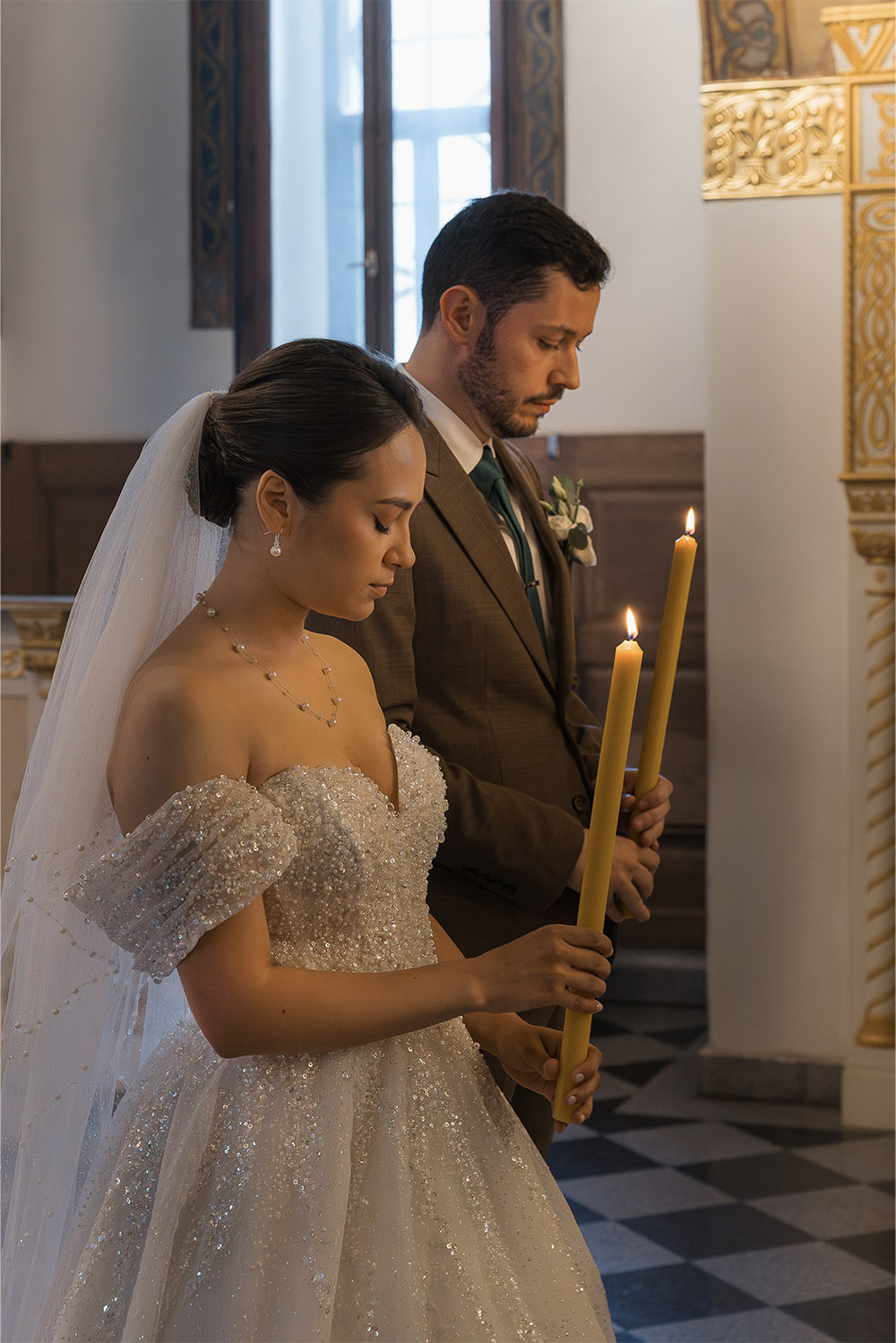 Inside Ružica Church at Kalemegdan Fortress in Belgrade, the bride and groom hold lit candles during their ceremony in a warm and intimate editorial wedding photograph.