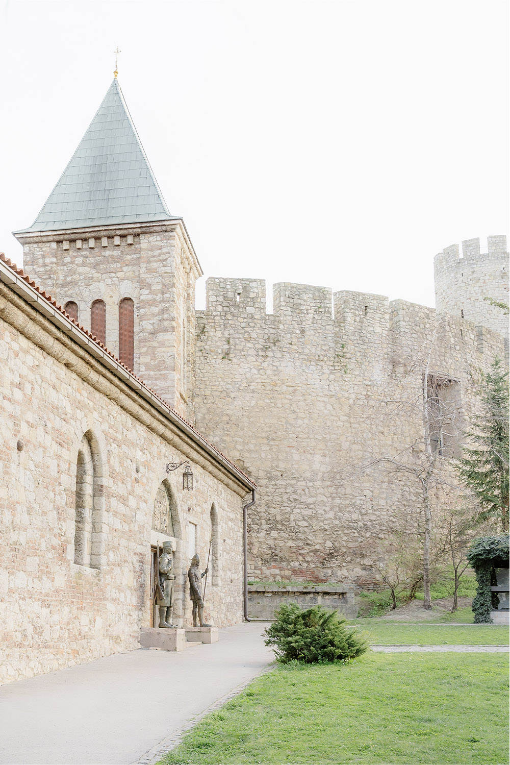 At Ružica Church within Belgrade’s Kalemegdan Fortress, the historic stone chapel stands beside ancient fortress walls in a bright editorial architectural wedding photograph.
