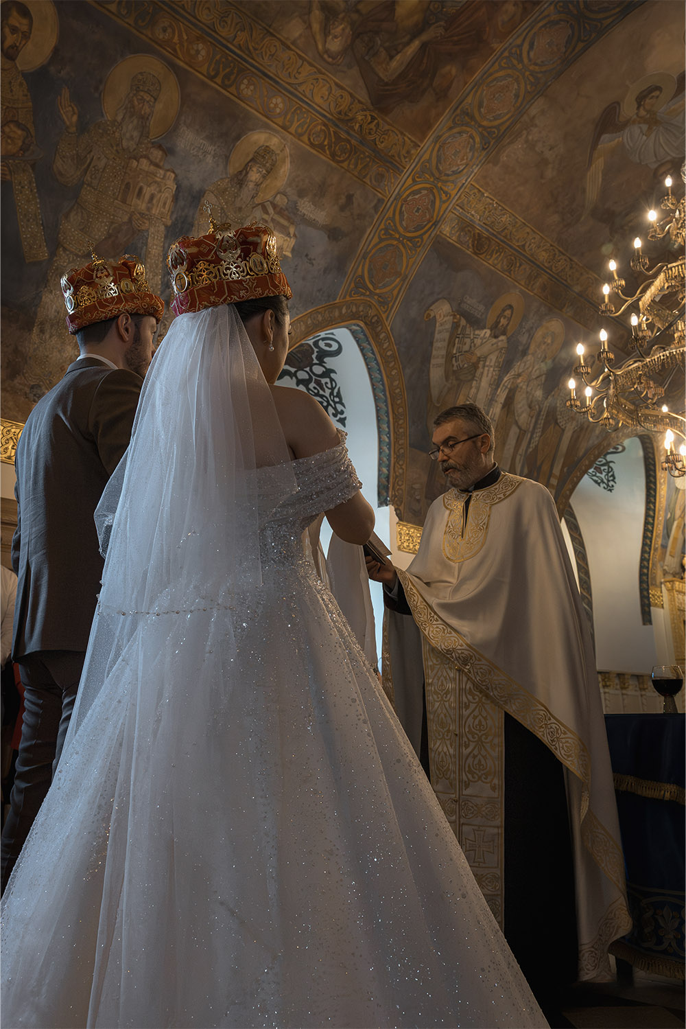 Inside Ružica Church at Kalemegdan Fortress, a priest officiates an Orthodox wedding ceremony for a crowned bride and groom in a richly detailed editorial photograph.