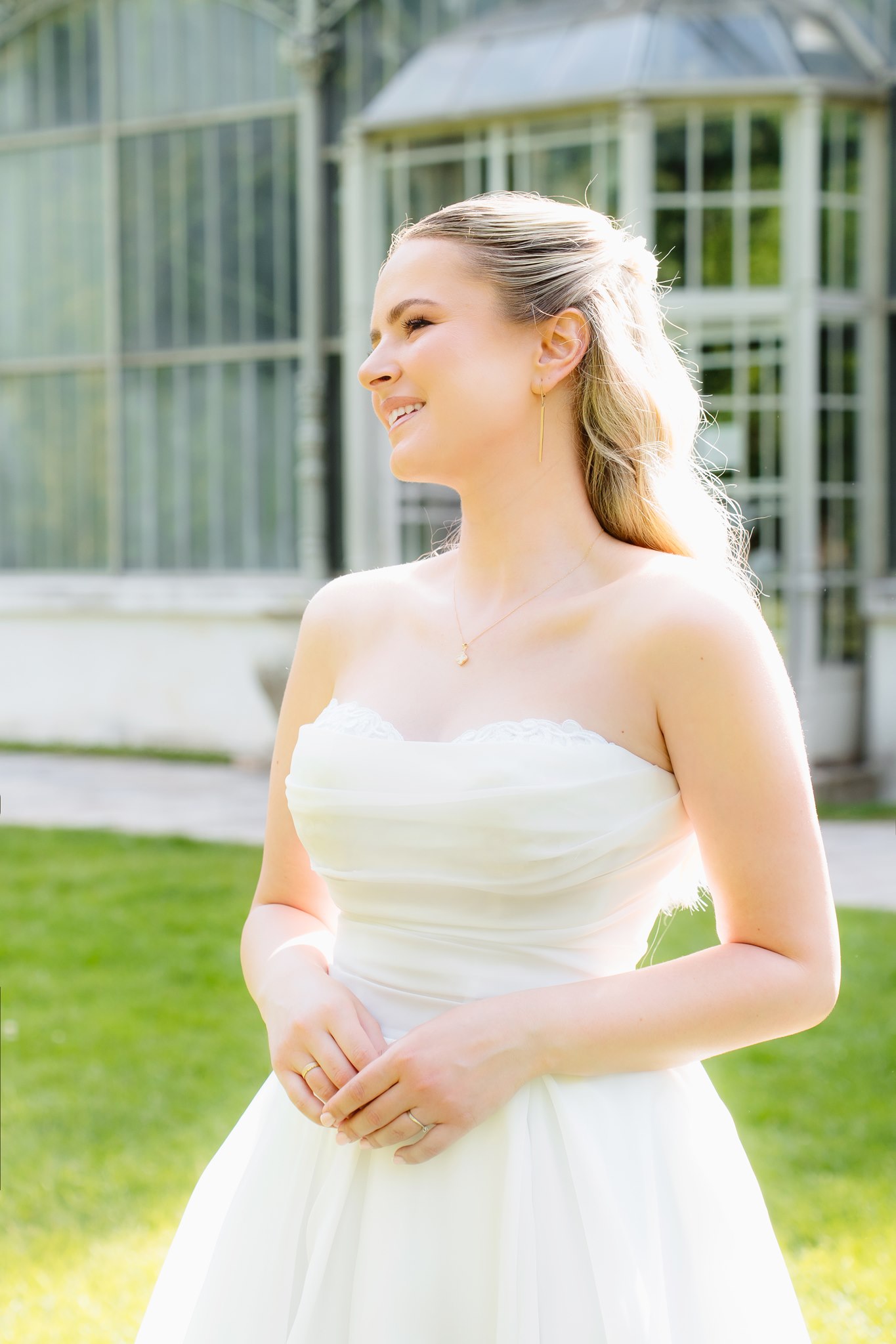 Photoshoot in Jevremovac Botanical Garden, Belgrade | Editorial Post-Wedding Photography 18 Editorial close-up of the bride standing in golden sunlight in front of the botanical garden greenhouse, smiling off-camera in a strapless gown with delicate lace neckline.