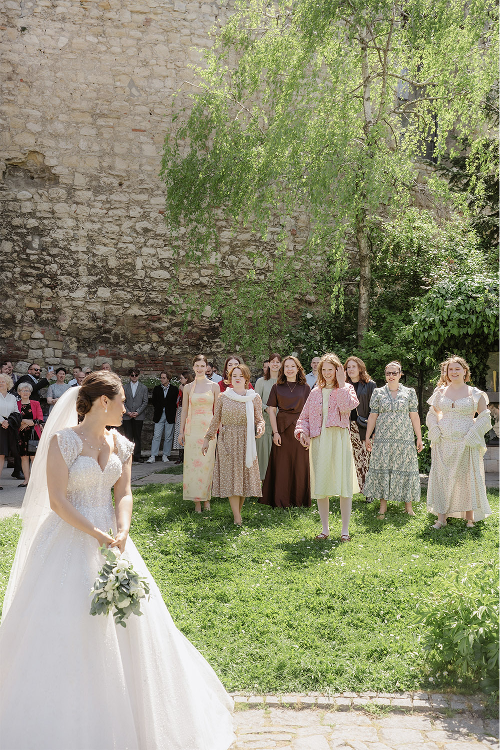 At Kalemegdan Fortress in Belgrade, the bride prepares to toss her bouquet as friends gather behind her on the lawn in a joyful editorial wedding photograph.