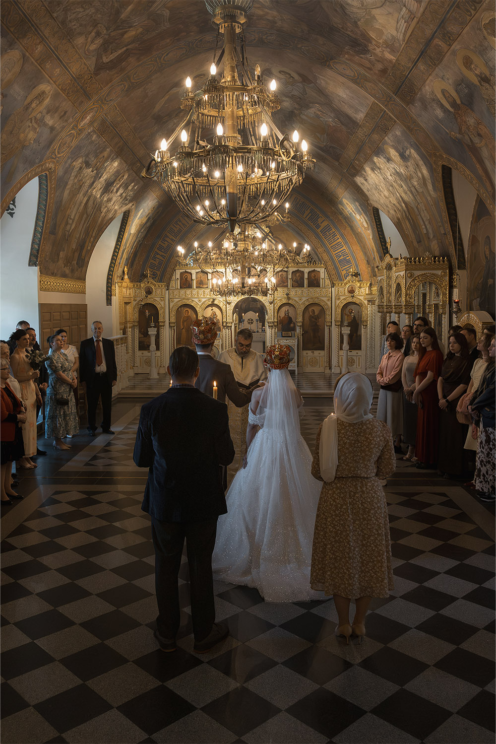 Inside Ružica Church at Kalemegdan Fortress, wedding guests gather around a crowned bride and groom as the priest leads the Orthodox ceremony in a dramatic editorial photograph showcasing the ornate interior.