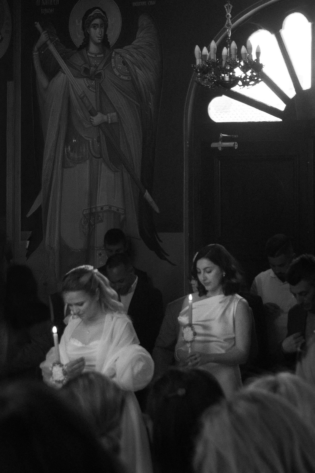 MIJO WEDDINGS 30 Inside an ornate church during a wedding ceremony, the bride and maid of honor hold candles among gathered guests in a softly lit editorial-style image that feels intimate and reverent.