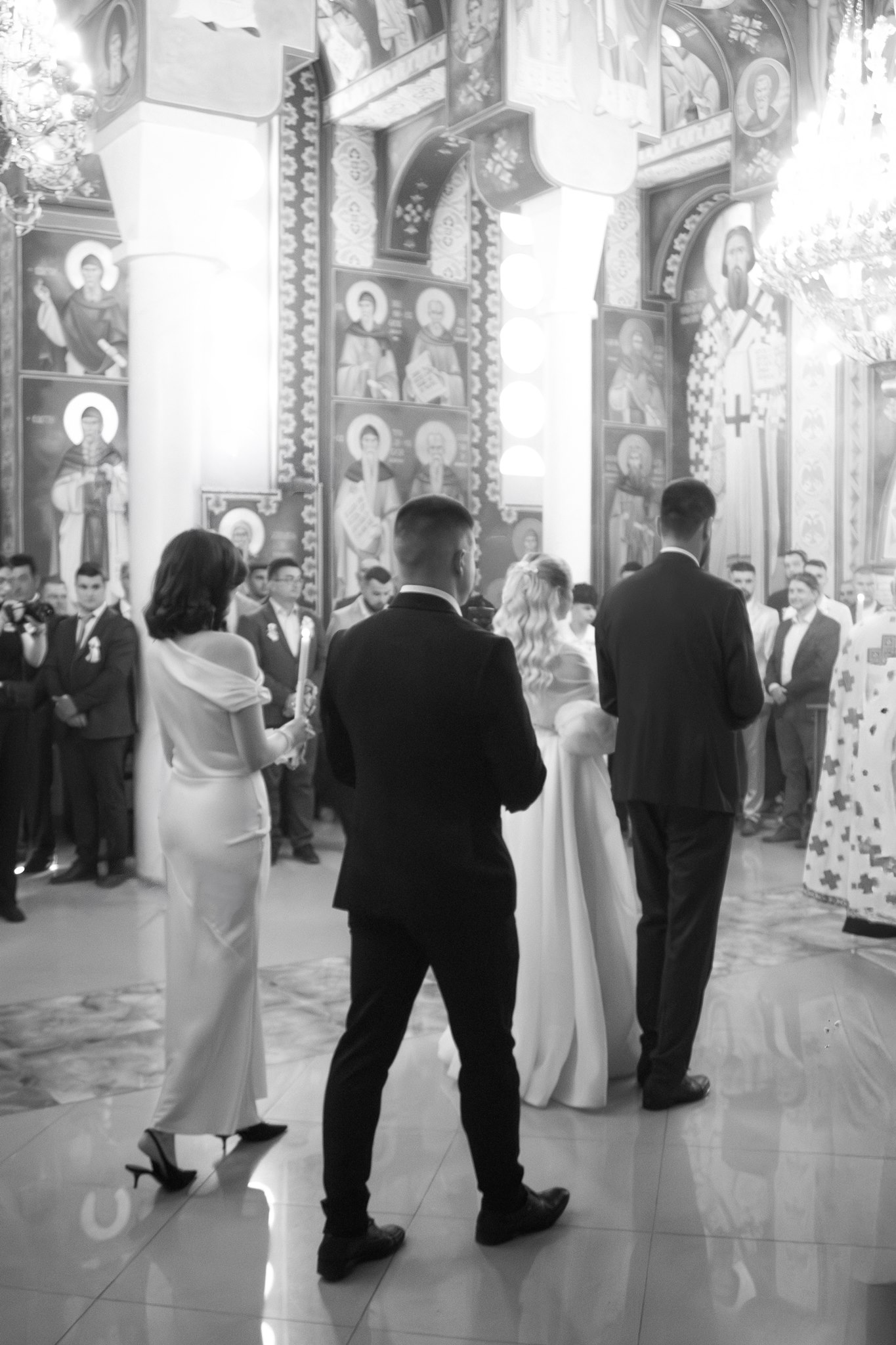 MIJO WEDDINGS 19 In a grand church adorned with religious artwork and chandeliers, a bride and groom stand before the altar during their ceremony in a timeless editorial-style wedding photograph.