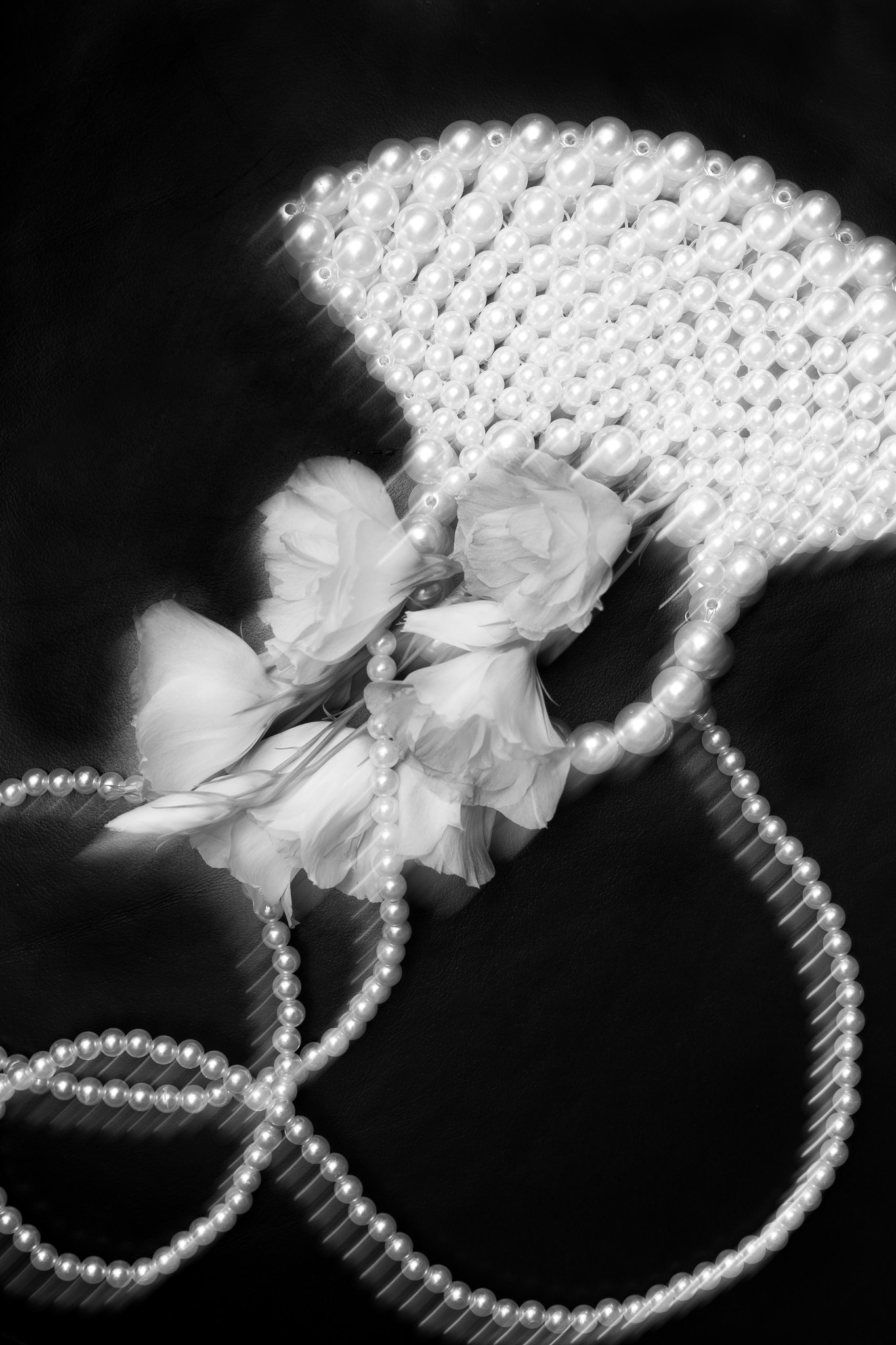 MIJO WEDDINGS 35 Against a dark backdrop, strands of pearls and delicate white flowers are artfully arranged in an editorial-style detail photograph highlighting texture, elegance, and romance.