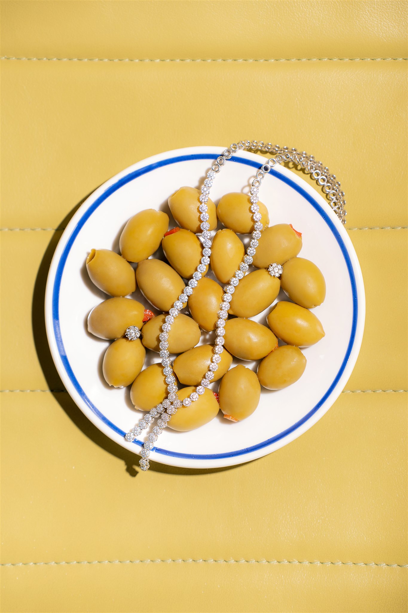 MIJO WEDDINGS 28 On a plate of green olives set against a soft yellow background, sparkling jewelry is styled as a contemporary editorial photograph that blends luxury with unexpected still-life storytelling.