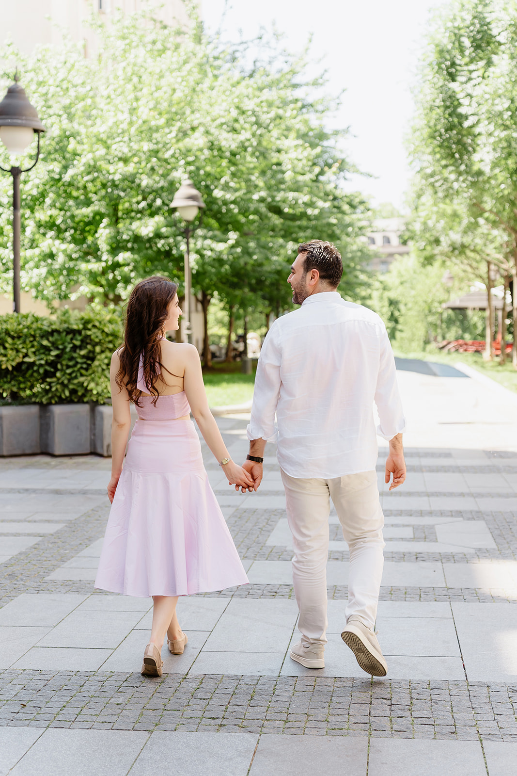 Editorial engagement photo of a couple holding hands and walking along a tree-lined street in central Belgrade on a sunny summer day.