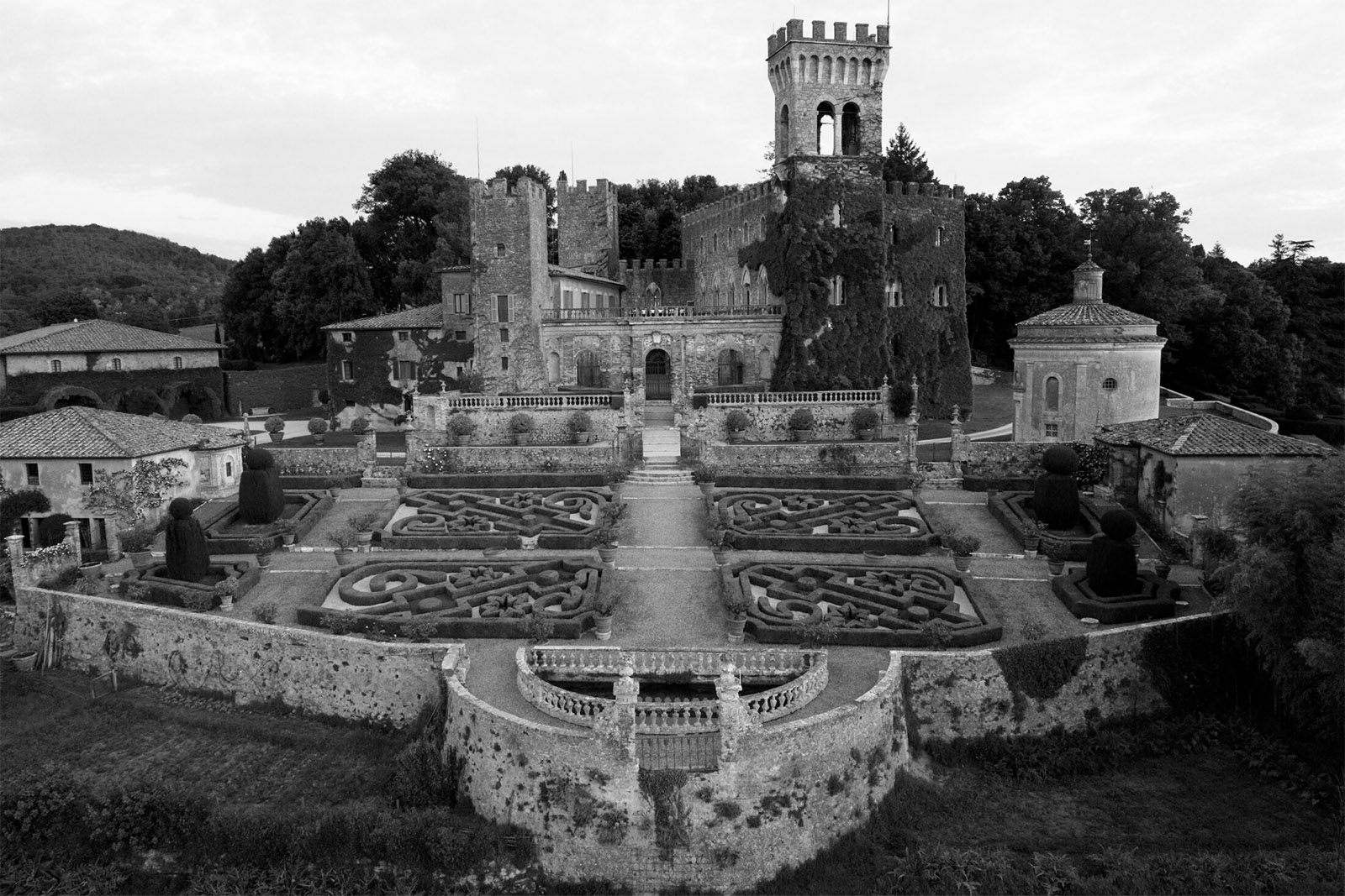 An editorial aerial view of Castello di Celsa in Tuscany, Italy, highlighting the medieval castle and its symmetrical Italian gardens.