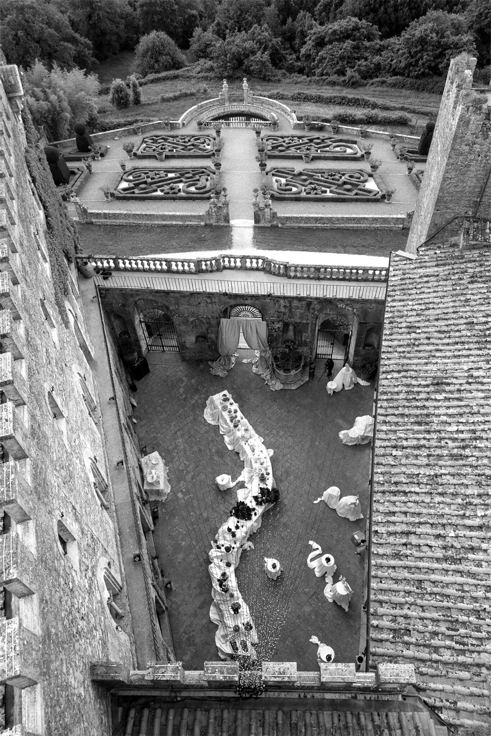 An editorial overhead view of Castello di Celsa in Tuscany, Italy, featuring the castle courtyard prepared for a wedding reception with a sweeping curved banquet table.